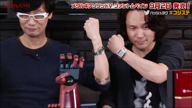 Hideo Kojima and Yoji Shinkawa raise their wrists to show their silver digital watches.