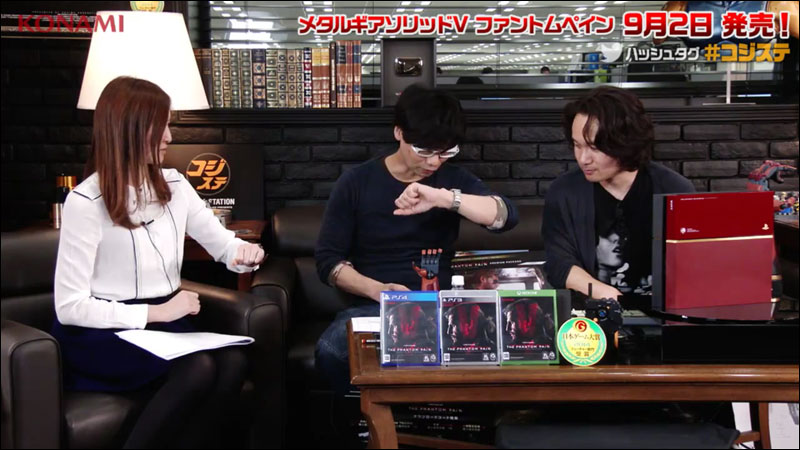 Kojima and Shinkawa sit behind Metal Gear merchandise and examine a wristwatch.