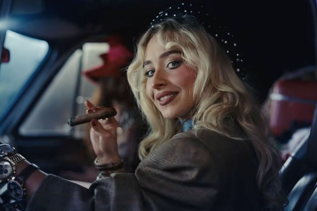 Sabrina Carpenter turns from the driver’s seat with several watches visible along her extended arm.