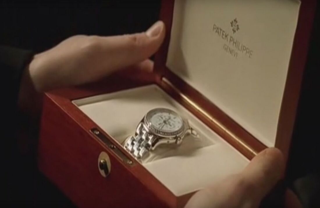 Hands hold an open red presentation box containing a diamond-set watch.