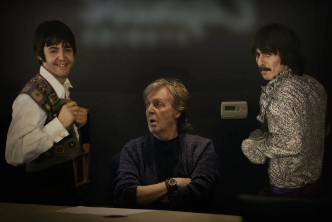 Paul McCartney sits with folded arms and a dark-dial watch on his right wrist, beside archival images of the younger Beatles.