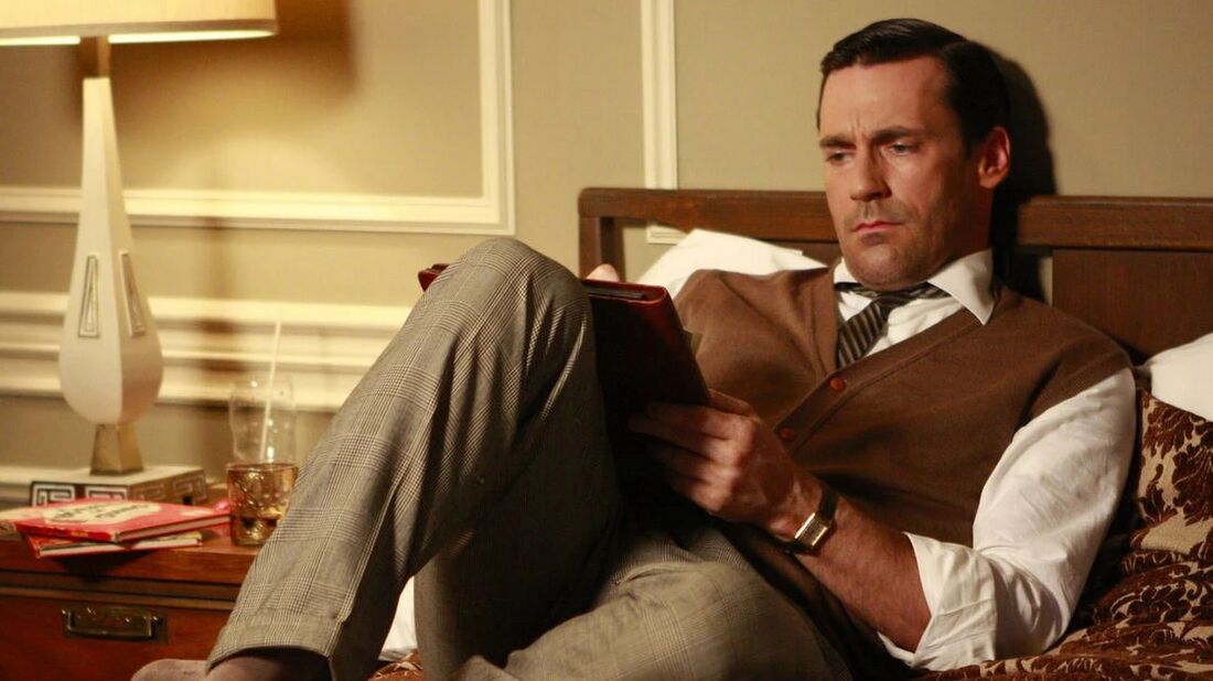 Don reclines on a bed reading a book, a rectangular watch at his left cuff.