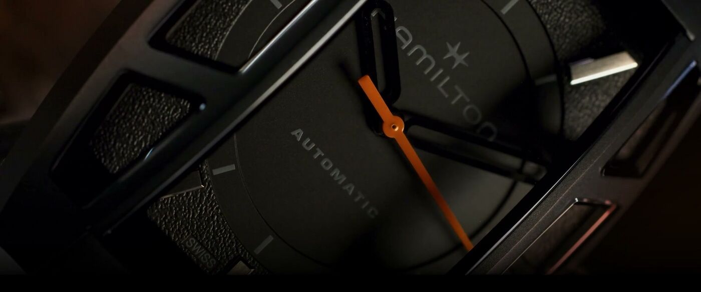 Close view of a black Hamilton watch with an orange seconds hand and separate crystal windows.