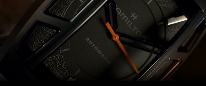 Close view of a black Hamilton watch with an orange seconds hand and separate crystal windows.