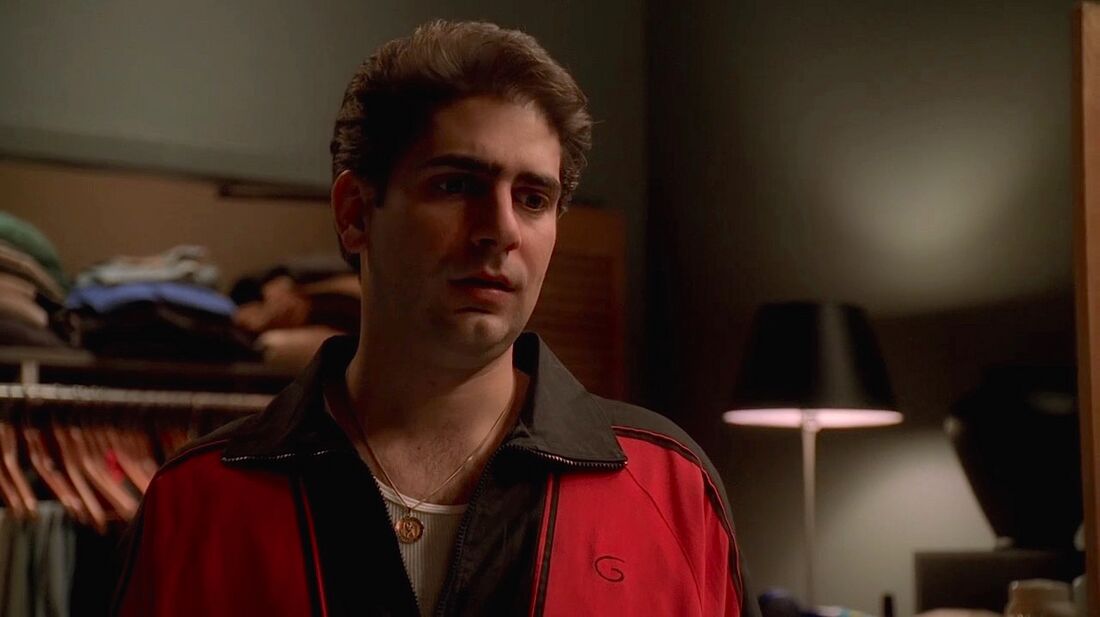 Christopher stands in a room wearing a red-and-black tracksuit jacket.