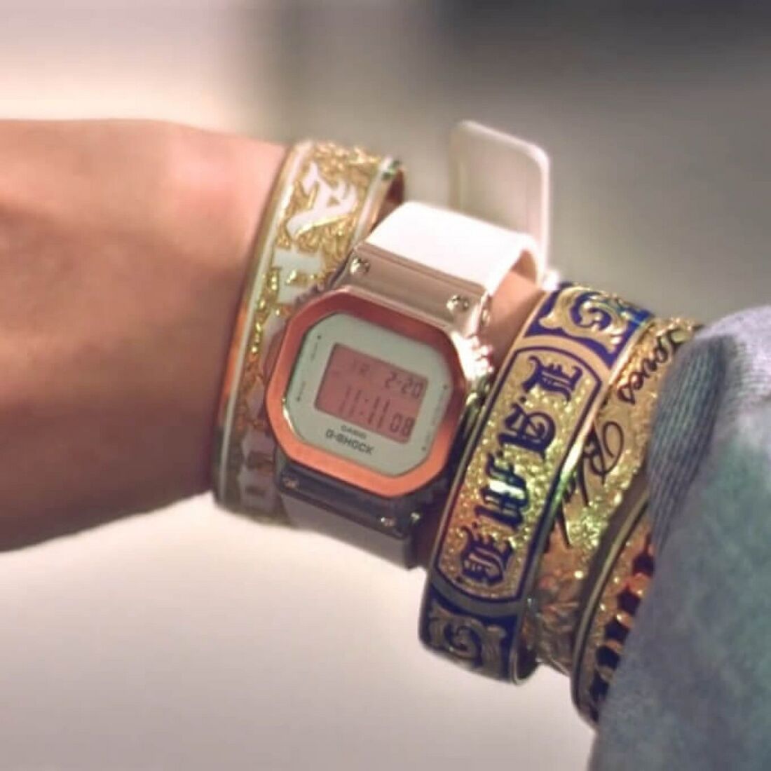 A square G-Shock with a pale strap sits between ornate bracelets.